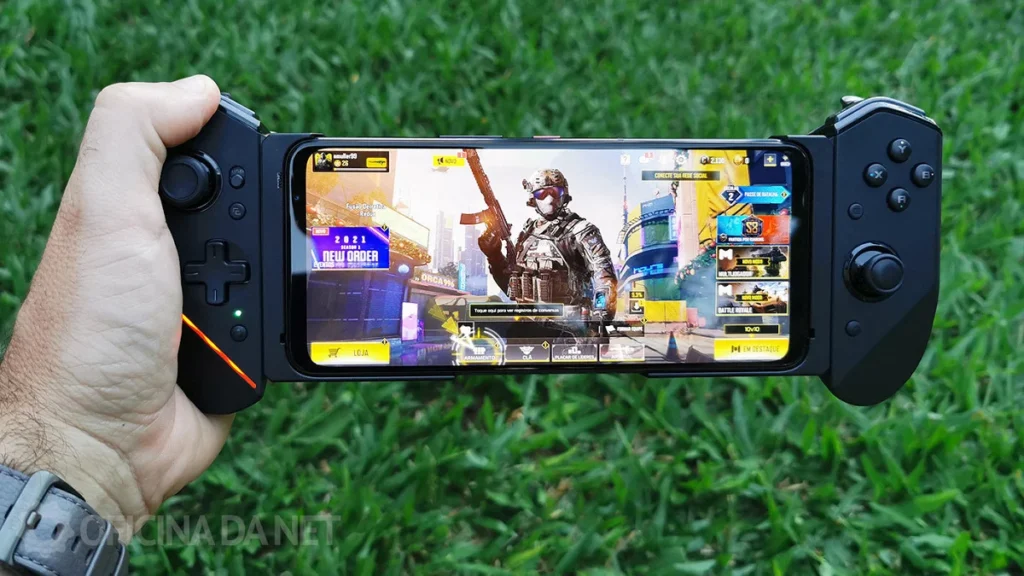 Mão segurando um smartphone na horizontal com um controle gamer preto acoplado nas laterais, rodando o menu do jogo Call of Duty Mobile, ilustrando a experiência competitiva dos melhores jogos para Android em 2026.